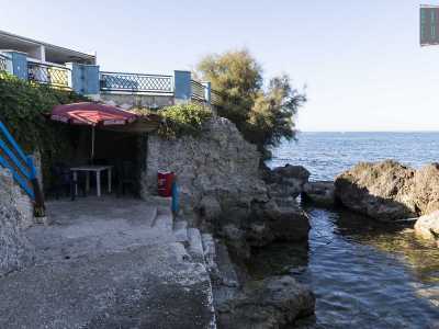 Usciamo dalla sala e scendiamo gi� al mare attraverso una scaletta. Siamo su una piattoforma di cemento affacciata sull�acqua e sulla quale si trova una cavit� naturale che ospita un ombrellone, un tavolino in plastica e delle sedie. Probabilmente si trattava della postazione del bagnino o di un angolo riservato alla docce